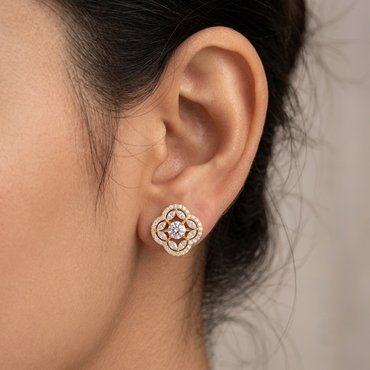 Model wearing a yellow gold quatrefoil halo stud earring featuring a central round diamond encircled by marquise diamonds and an outer scalloped pavé halo, shown in its exact size on the earlobe.