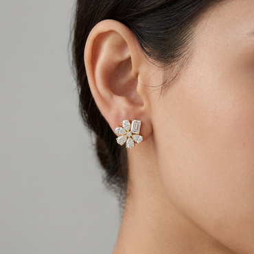 Model wearing a yellow gold floral stud earring featuring pear-cut diamond petals and an accent baguette-cut diamond at the top, shown close-up on the earlobe.