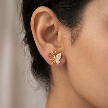 Model wearing an asymmetrical yellow gold butterfly stud earring featuring one pavé diamond-paved wing and one openwork gold wire wing, shown close-up on the earlobe.