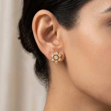 Model wearing a yellow gold floral star stud earring featuring a central round diamond surrounded by six gold petal frames with solitaire diamond centers, shown close-up on the earlobe.