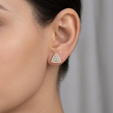 Model wearing a yellow gold trillion-cut diamond stud earring enclosed in a double pavé diamond halo frame, shown close-up on the earlobe.