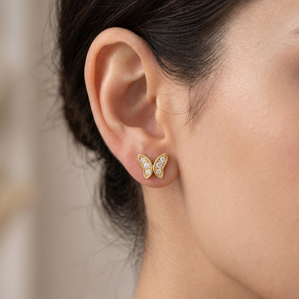 Model wearing a yellow gold butterfly stud earring featuring pavé diamond-set wings framed in smooth gold borders, shown in its exact size on the earlobe.