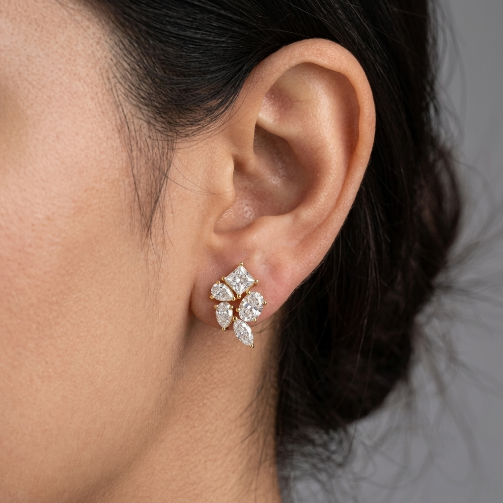 Model wearing a yellow gold multi-shape diamond cluster stud earring featuring a top princess-cut diamond anchored by pear, oval, and marquise-cut diamonds, shown in its exact size on the earlobe.
