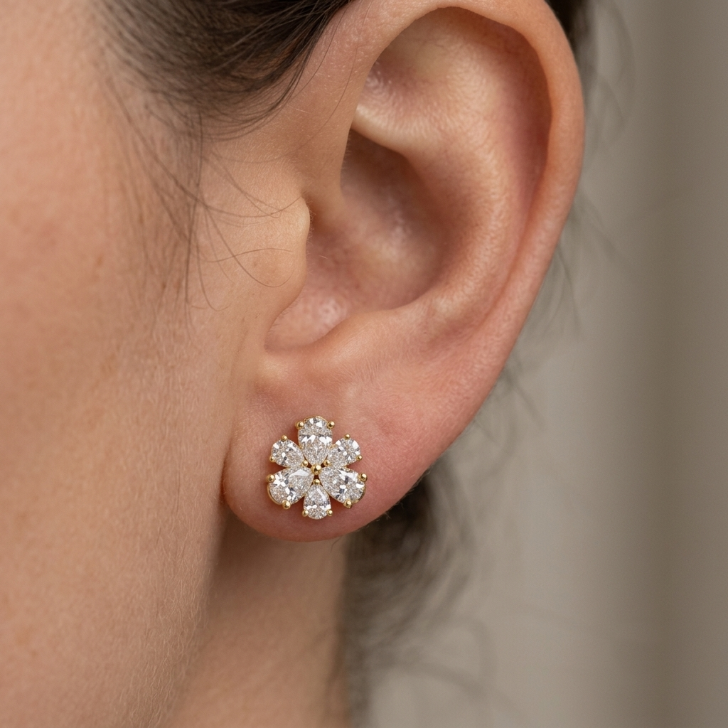 Model wearing a yellow gold floral stud earring featuring six pear-cut diamonds arranged as petals around a central accent diamond, shown in its exact size on the earlobe.
