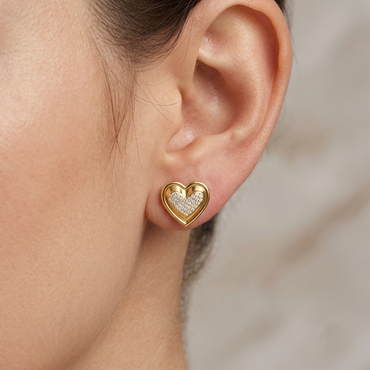 Model wearing a yellow gold heart-shaped stud earring featuring a pavé diamond-encrusted center framed by polished gold outer borders, shown close-up on the earlobe.
