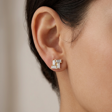 Model wearing a yellow gold square stud earring featuring four interlocking baguette-cut diamonds arranged in a geometric pinwheel pattern, shown close-up on the earlobe.