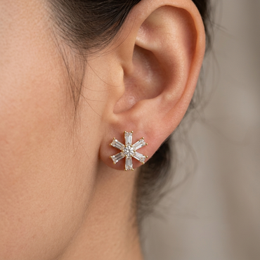 Model wearing a yellow gold starburst stud earring featuring radiating baguette-cut diamonds surrounding a central round solitaire diamond, shown close-up on the earlobe.