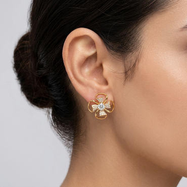 Model wearing a yellow gold swirl floral stud earring featuring a central round diamond surrounded by four pavé-set diamond petals and open gold loops, shown close-up on the earlobe.