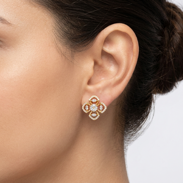 Model wearing a yellow gold four-leaf clover stud earring featuring a central round diamond cluster framed by pavé-set diamond openwork petals, shown close-up on the earlobe.