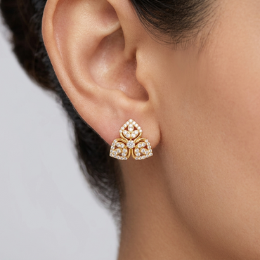 Model wearing a yellow gold floral trifoil stud earring featuring three pavé diamond-encrusted leaf petals centered around a round diamond cluster, shown close-up on the earlobe.