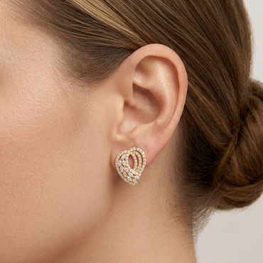 Model wearing a yellow gold swirl stud earring set with pave diamonds in concentric sweeping ribbons, shown close-up on the earlobe.